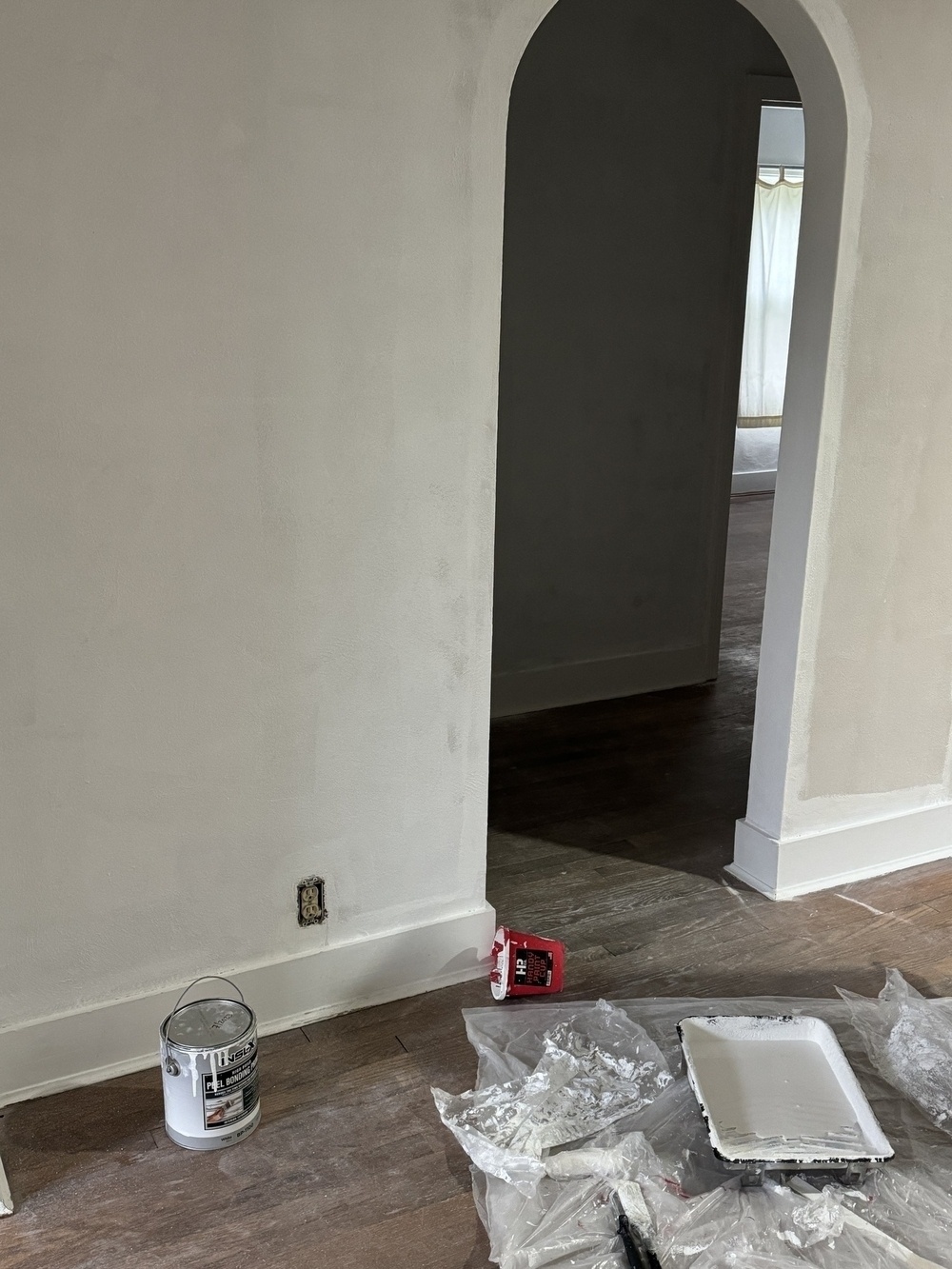 A wall with paint primer on it, an archway, and a floor covered in painting supplies.