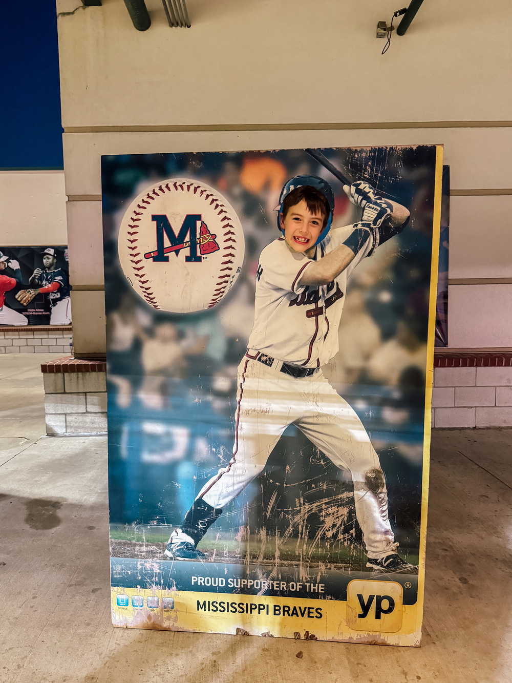 A boy smiling through a photo cutout of a baseball player