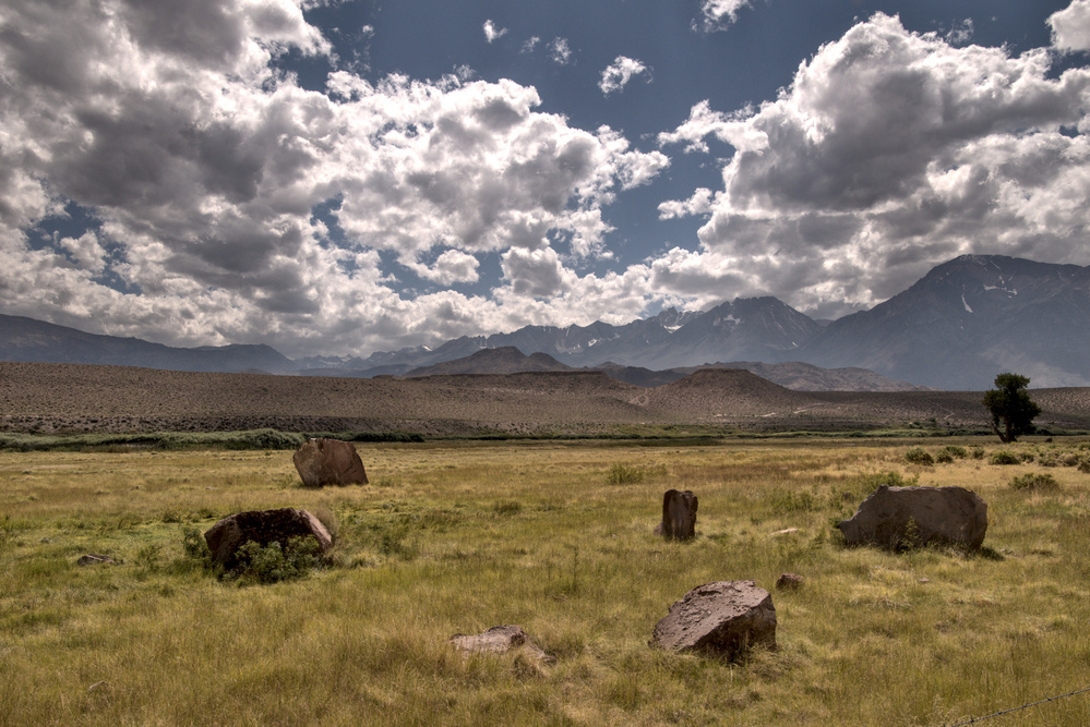 Five blocks of pink stone lie at random in marshy grass, with mountains in the distance. the sky full of puffy clouds.