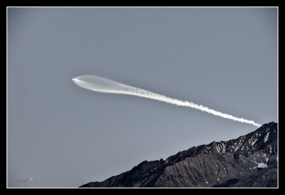 A rocket exhaust plume rises from the top of a mountain,