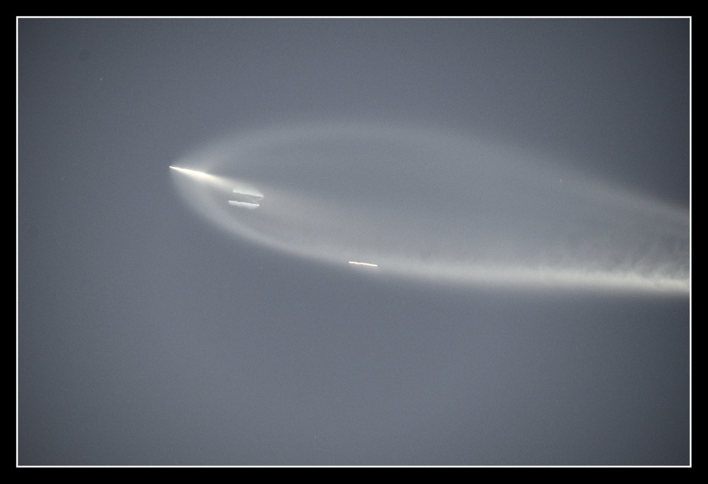 Closeup of the rocket plume, with three bright lines trailing behind the rocket.