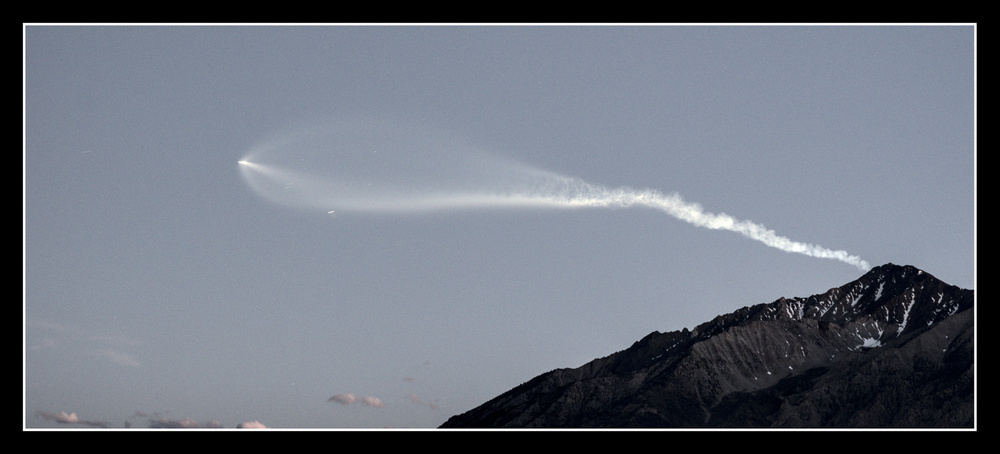 Wide  view of the rocket and mountain, a bit later, the rocket is further and the contrail is beginning to disperse.