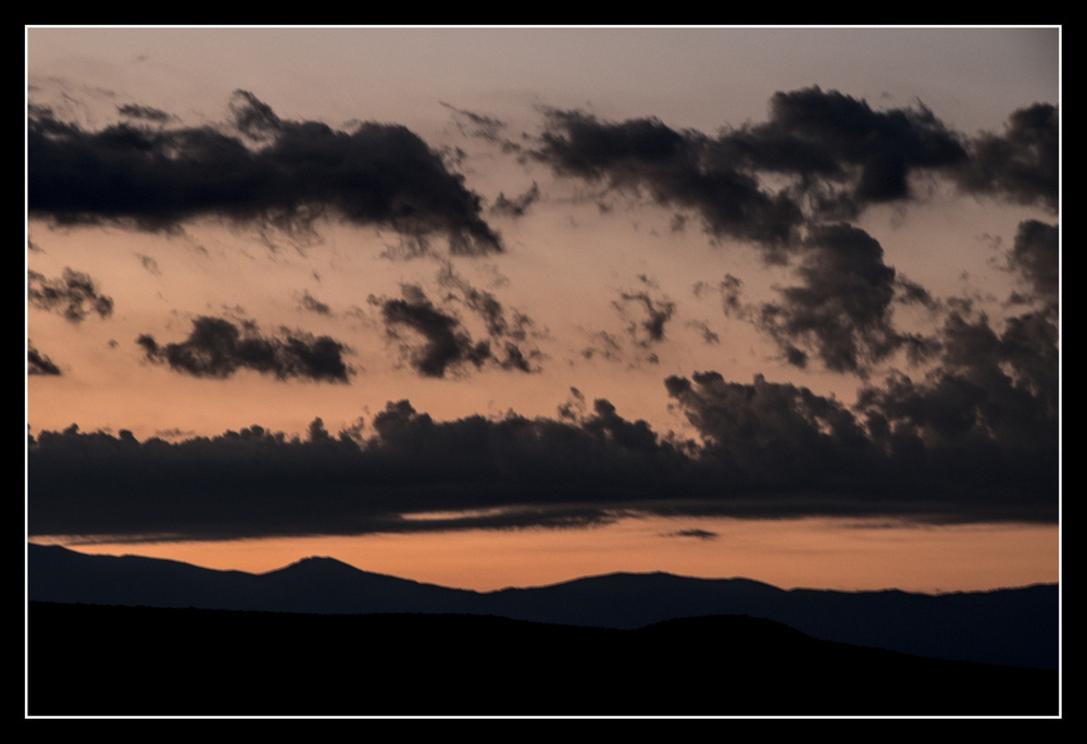 Clouds are scattered against a dim orange sky above a dark mountain range.