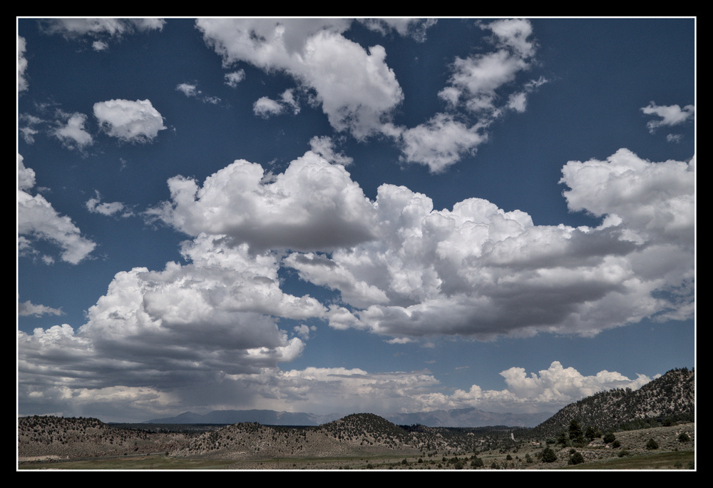 Above parched, sage desert, the deep blue sky is full of white cumulonimbus clouds.