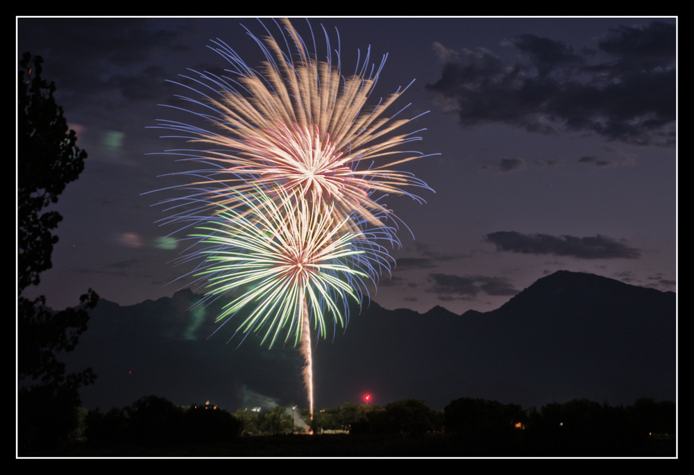 Fireworks launch from a city park
     with large mountains visible behind.