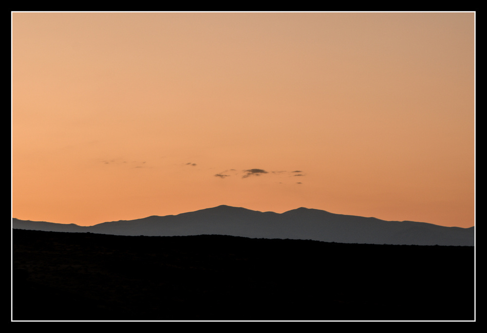 An orange sky before sunrise has just a few clouds. The silhouettes of hills and mountains run below.