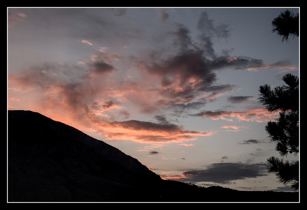 Clouds over the shoulder of a mountain ridge turn pink with the sunset.