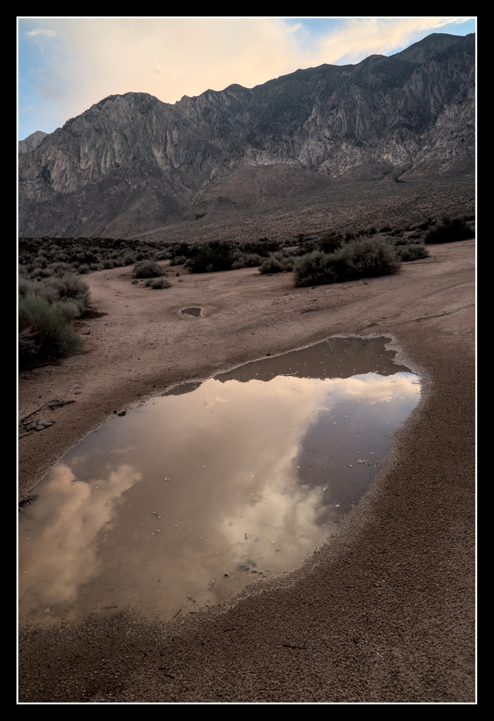 A large puddle in a dirt road reflects a large granite mountain.