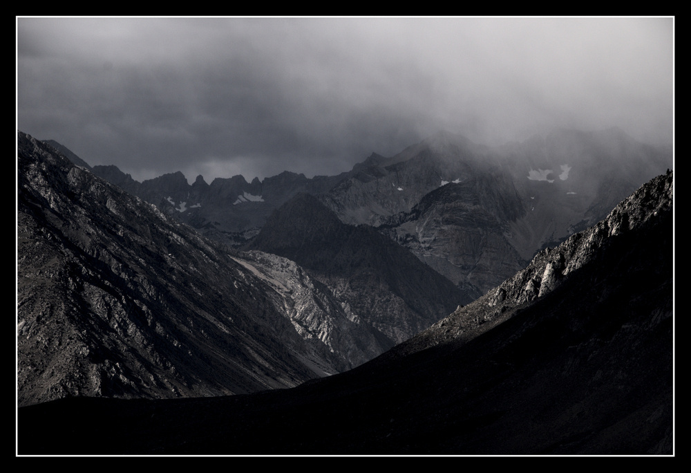 A dark grey cloud bank hovers over a canyon running deep into jagged mountains.