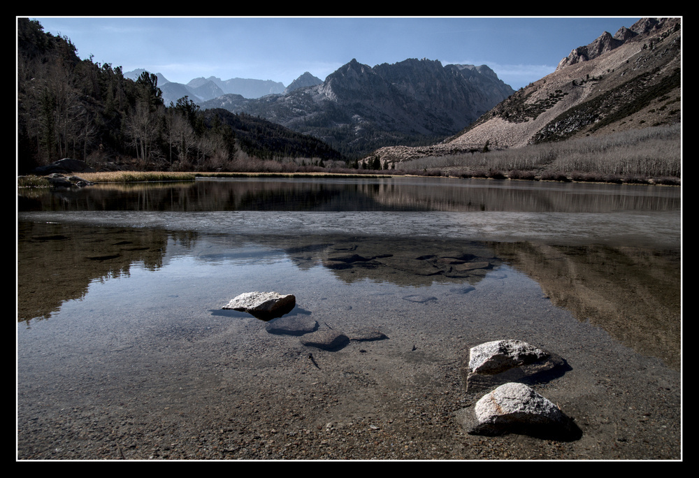 A few rocks stick out of the water near the shore of a mountain lake.