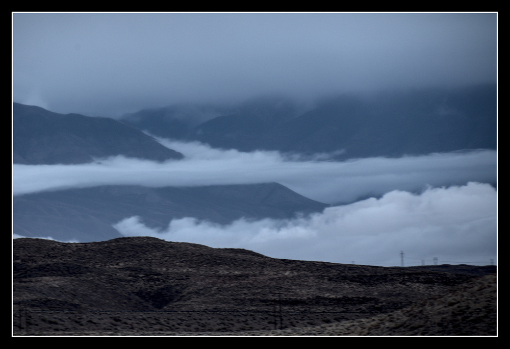 Low lying clouds curve through rounded hills.