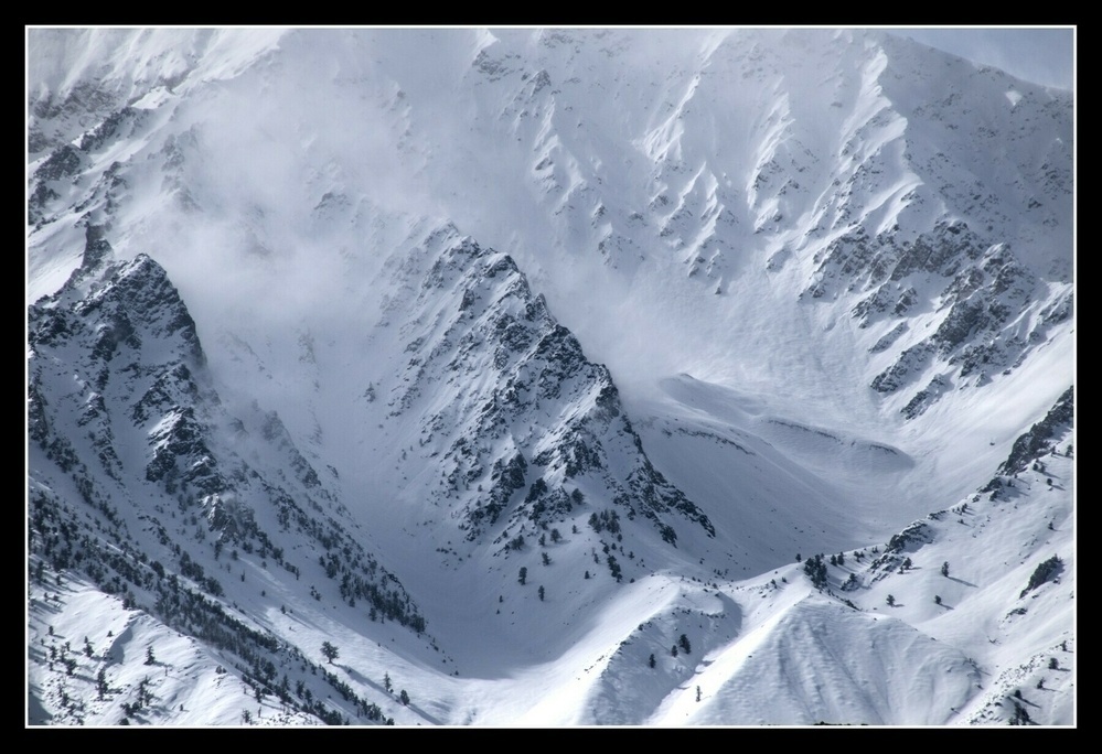 A sharp ridge , like a flint arrowhead, stands out from a canyon on a mountain top, covered in fresh snow.