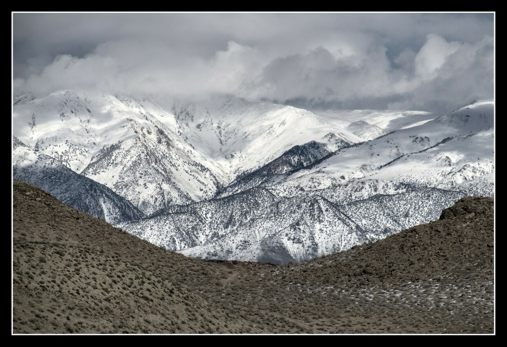 A curved bluff below and clouds above frame a remote mountain peak.