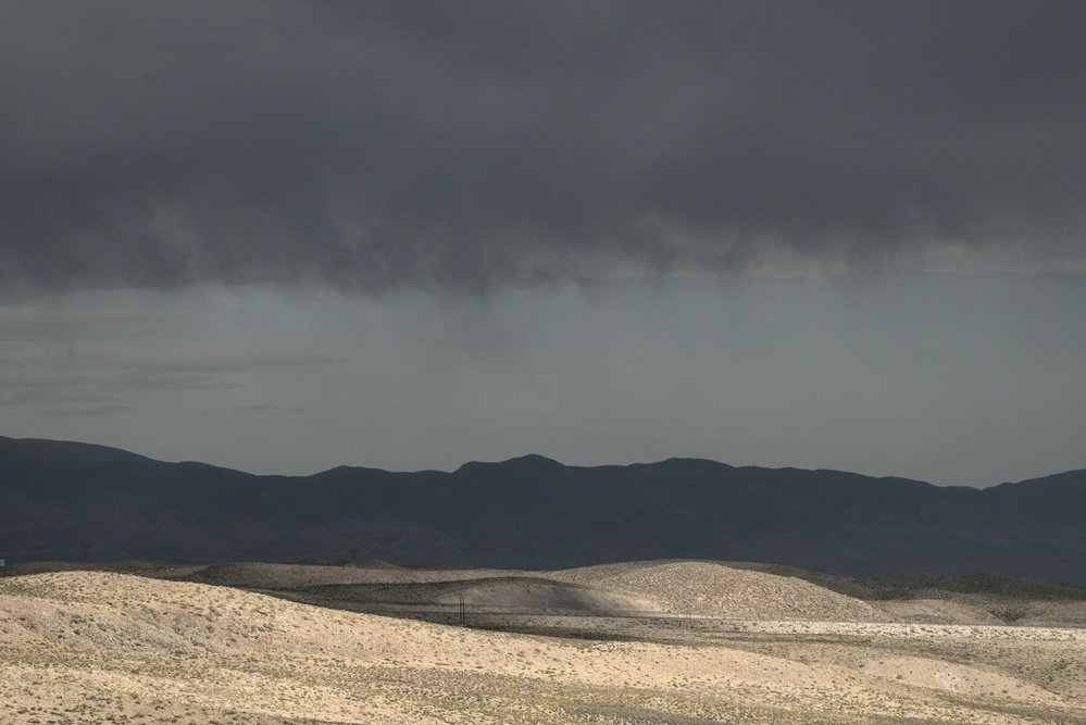 Sun on the high desert contrasts with the deep shadow of a storm behind.
