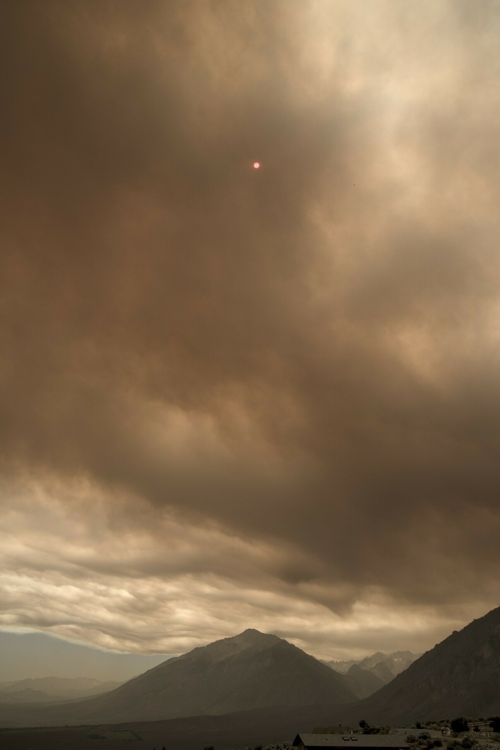 A dark plume of smoke fills the sky and discolors the sun.