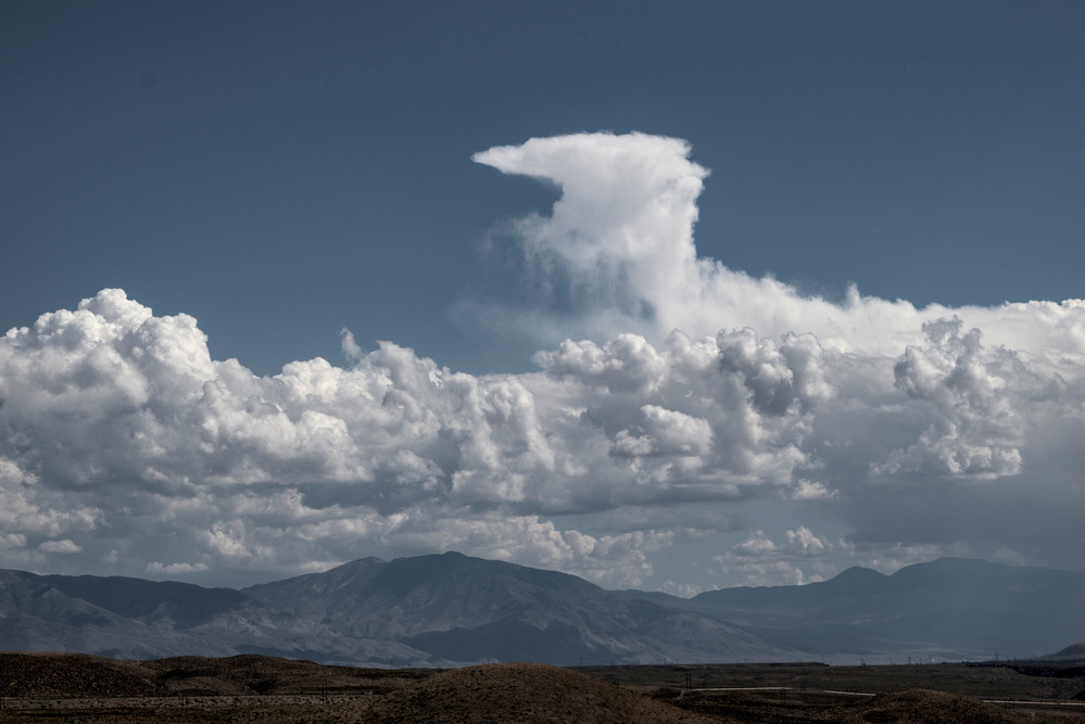 An odd sheped cloud rises from a long bank of low-lying cumulonimbus clouds.