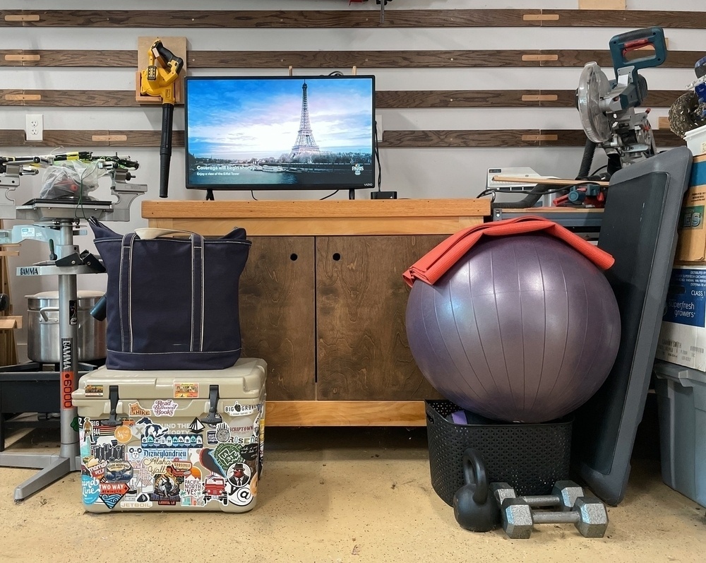 A collection of junk in the garage (cooler, giant ball, workbench) with a TV waiting to start the evenings Olympics program