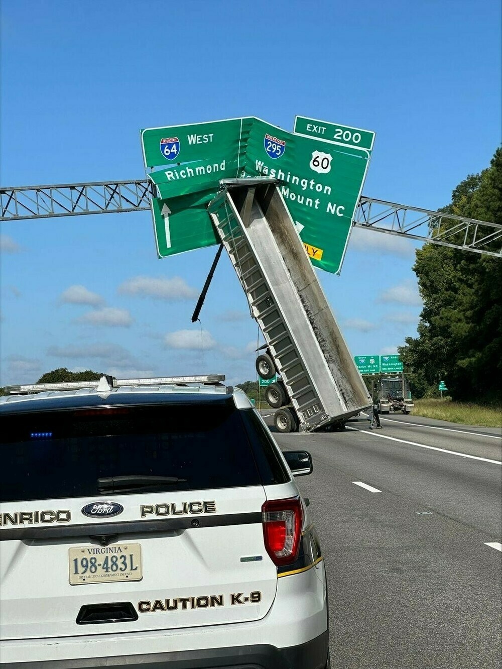 A tractor trailer flipped up into the highway sign above the road