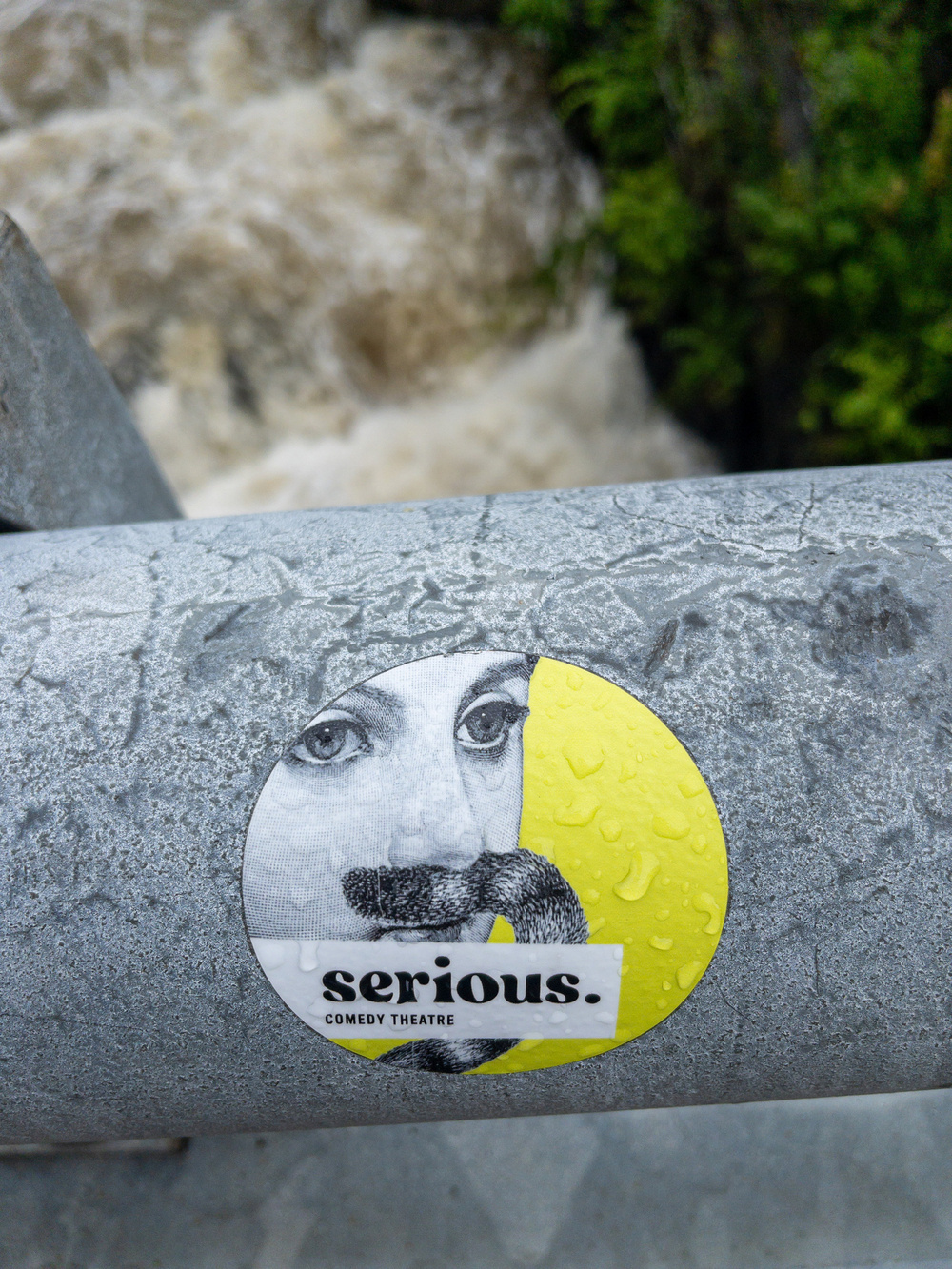 Sticker on railing depicting a feminine face with a cat’s tail mustache and the words serious comedy theater.