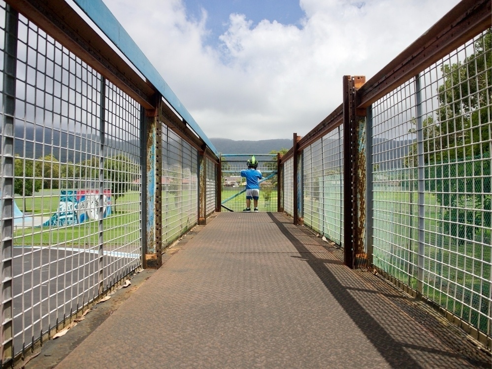 Looking down the length of an old viewing platform at a young boy observing people below