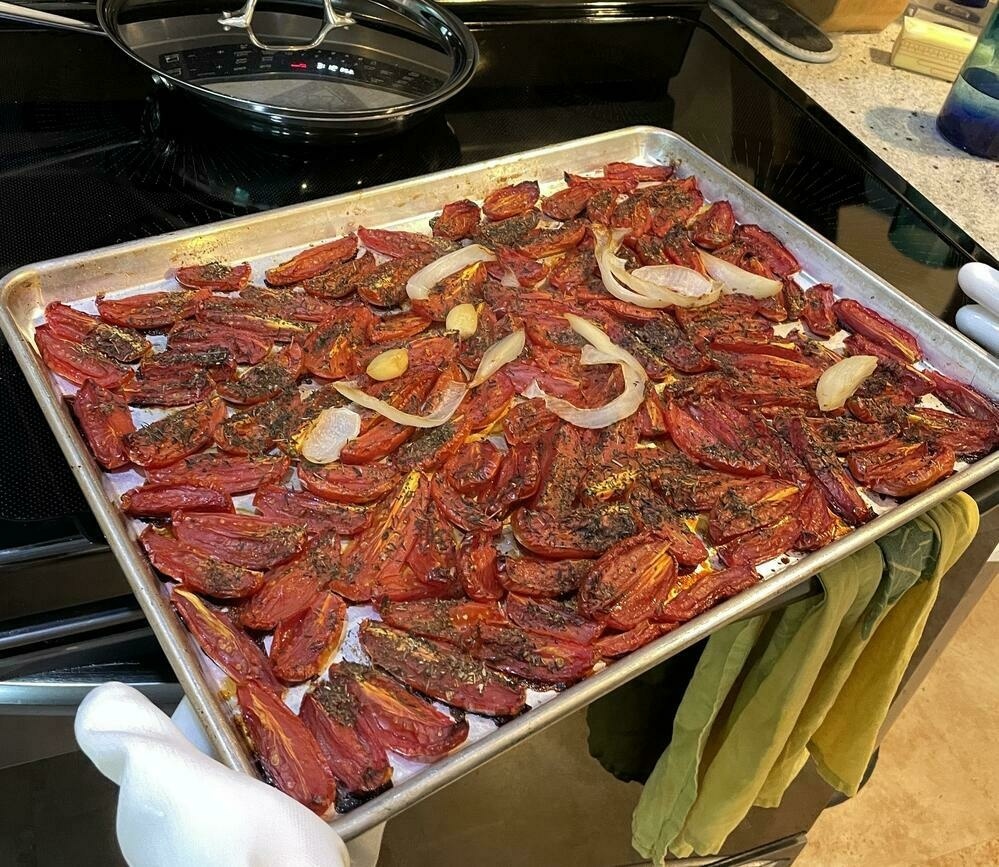 Pan of partially roasted Roma tomatoes during pan shelf rotation about to go back into the oven to continue roasting.