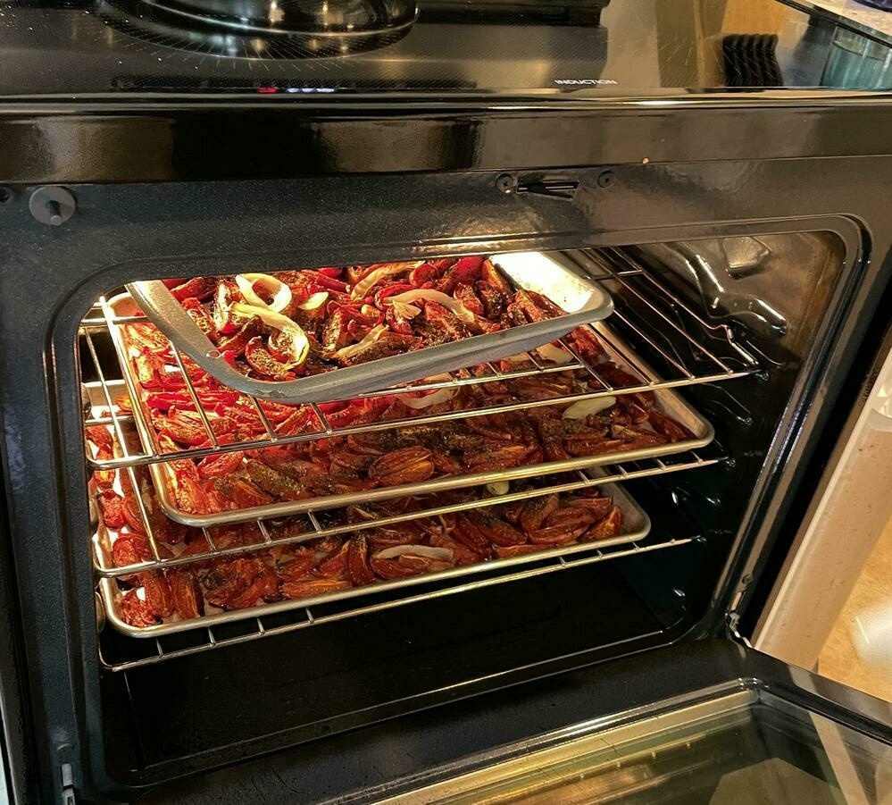 Oven full of pans of roasting Roma tomatoes on cookie sheets and in a  roasting pan.