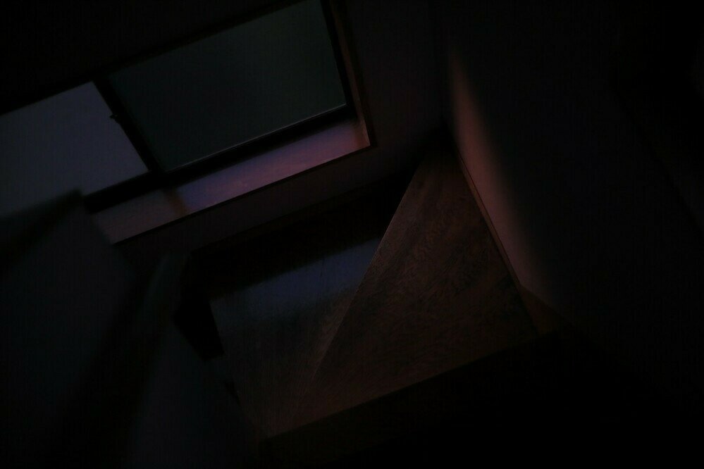 The corner of staircase. The dusk light is coming through the window and wooden stairs and the wall are dimly illuminated in red.