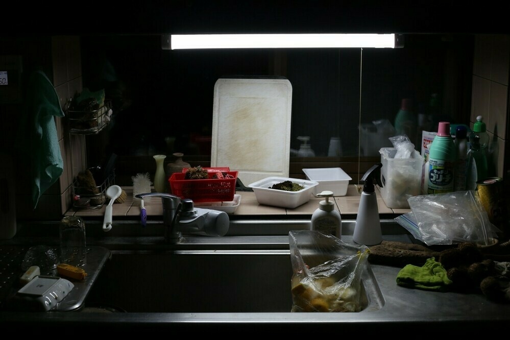 Fluorescent lights illuminate the cluttered kitchen.