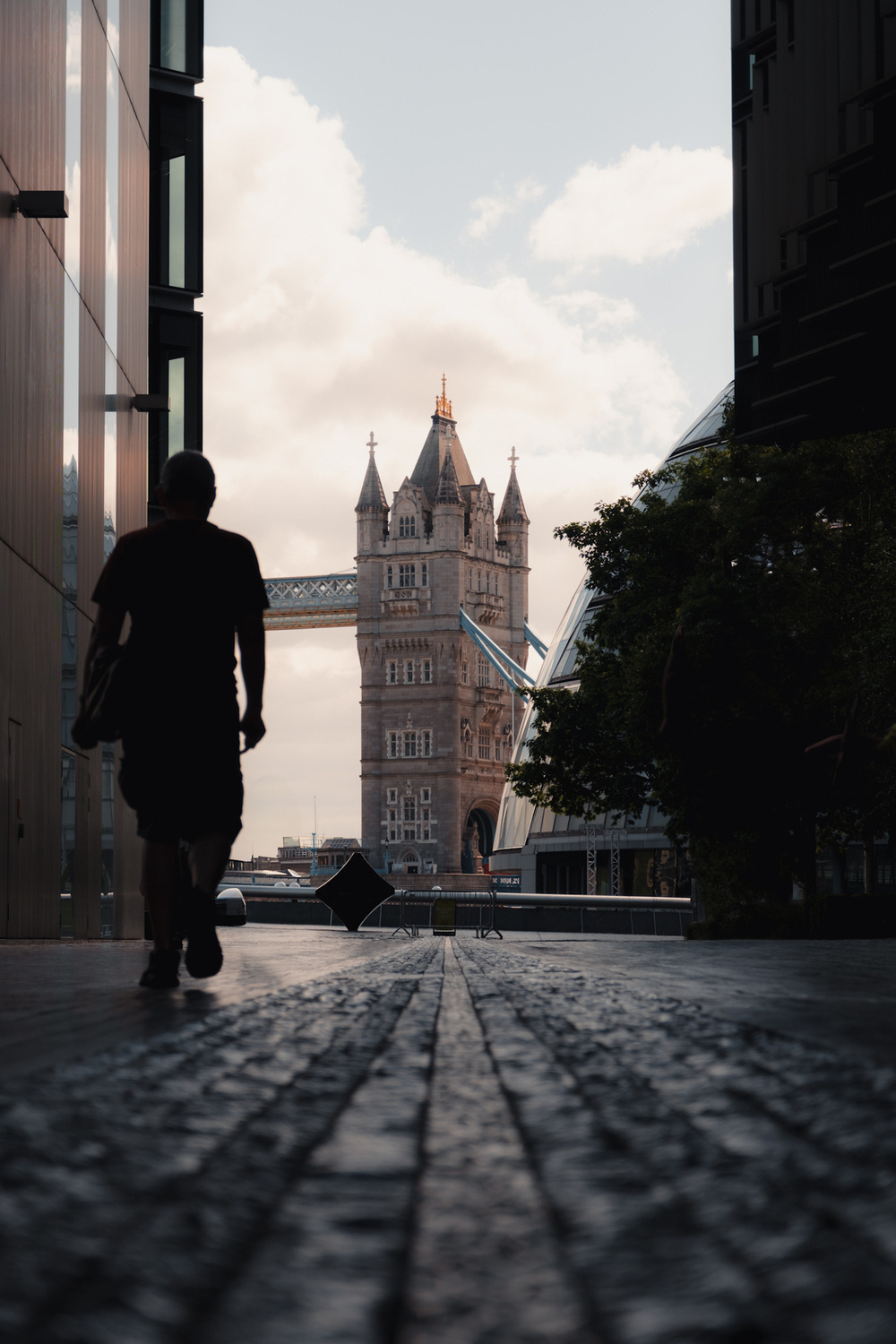 A person walks through a narrow passageway with the Tower Bridge prominently visible in the background.