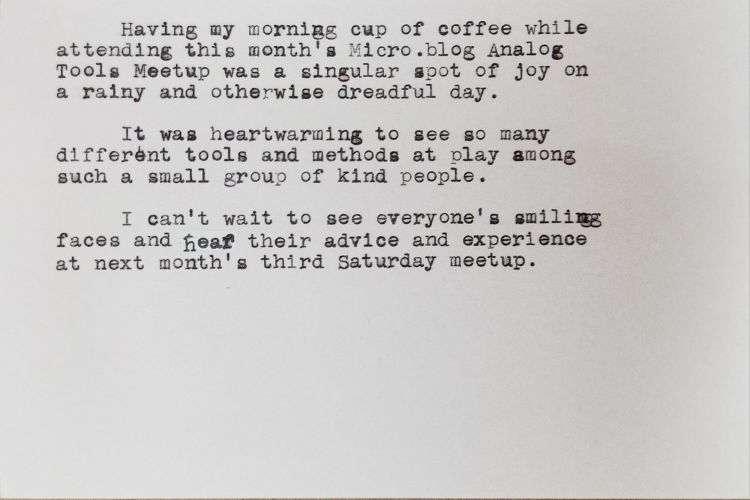 Typewritten index card that reads: "Having my morning cup of coffee while attending this month's Micro.blog Analog Tools Meetup was a singular spot of joy on a rainy and otherwise dreadful day. It was heartwarming to see so many different tools and methods at play among such a small group of kind people. I can't wait to see everyone's smiling faces and hear their advice and experience at next month's third Saturday meetup."