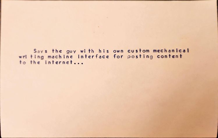 Typed index card that reads Says the guy with his own custom mechanical wri ting machine interface for posting content to the internet...