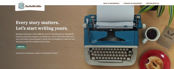 Hero image from the NaNoWriMo homepage featuring a view down onto a writing desk which has a blue 1960s Royal Safari typewriter, a coffee mug, and a red plate with a seeded bagel.