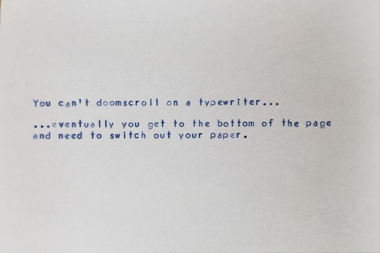 White index card with typewritten Vogue typeface in blue ink which reads: You can't doomscroll on a typewriter... ...eventually you get to the bottom of the page and need to switch out your paper.