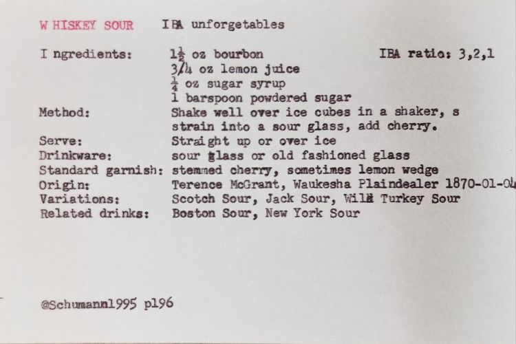 typed white index card that reads: WHISKEY SOUR IBA unforgetables; IBA ratio: 3,2,1; Ingredients: 1½ oz bourbon, 3/4 oz lemon juice, 1 oz sugar syrup, 1 barspoon powdered sugar; Method: Shake well over ice cubes in a shaker, s strain into a sour glass, add cherry. Serve: Straight up or over ice; Drinkware: sour glass or old fashioned glass; Standard garnish: stemmed cherry, sometimes lemon wedge; Origin: Terence McGrant, Waukesha Plaindealer 1870-01-04; Variations: Scotch Sour, Jack Sour, Wild Turkey Sour; Related drinks: Boston Sour, New York Sour; @Schumann1995 p196