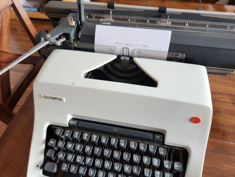 Index card in large font on a white Olympia SG-3 typewriter which reads "Once Upon a Time..."