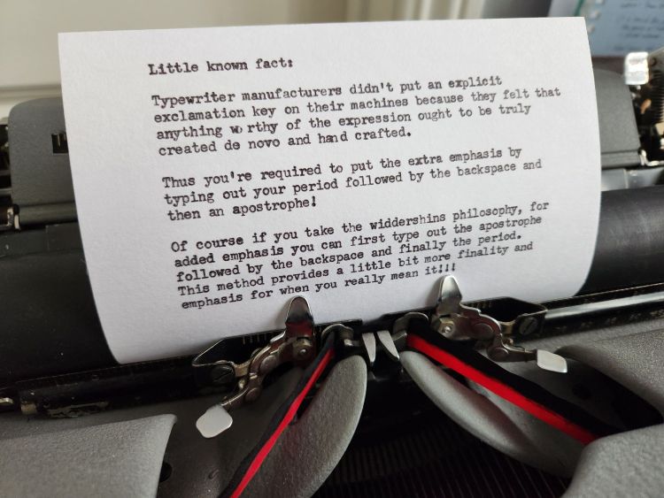 Typed 4 x 6" index card in the carriage of a grey typewriter with black/red ribbon. The card reads: "Little known fact: Typewriter manufacturers didnt put an explicit exclamation key on their machines because they felt that anything worth of the expression ought to be truly created de novo and hand crafted. Thus you're required to put the extra emphasis by typing out your period followed by the backspace and then an apostrophe! Of course if you take the widdershins philosophy, for added emphasis you can first type out the apostrophe followed by the backspace and finally the period. This method provides a little bit more finality and emphasis for when you really mean it!!!
