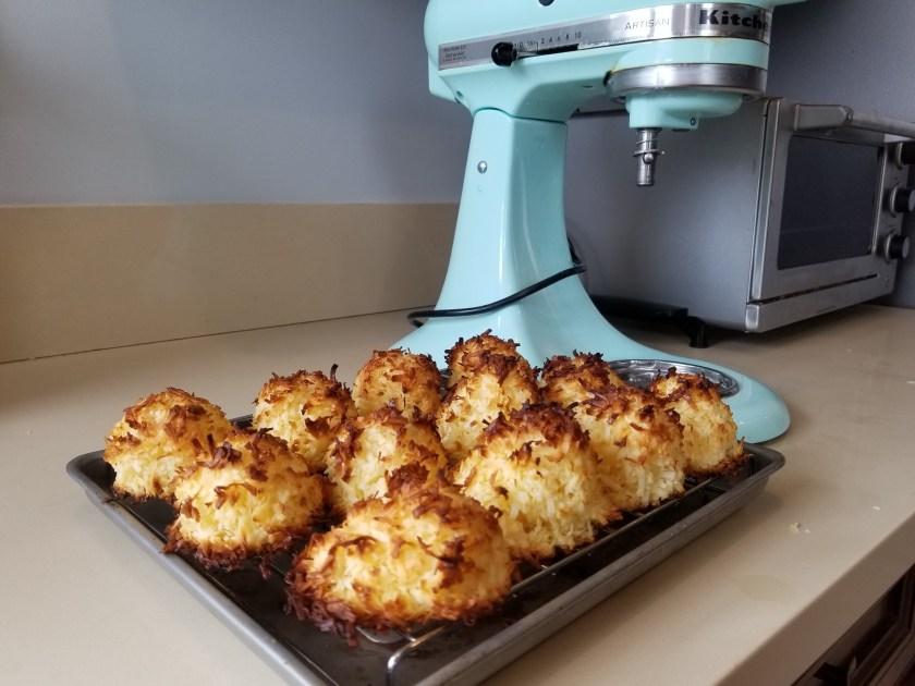 Well baked macaroons with browned edges on a cooling rack in the foreground and teal stand mixer in the background