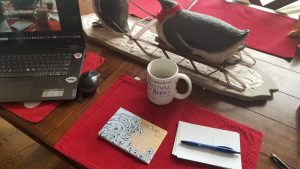 dining room table with penguin ornamental centerpiece, a laptop, postcards that read "We the People", coffee, and pens