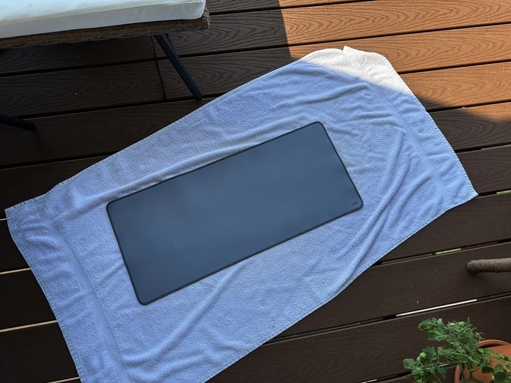 A gray deskpad laying on a towel in the shade.