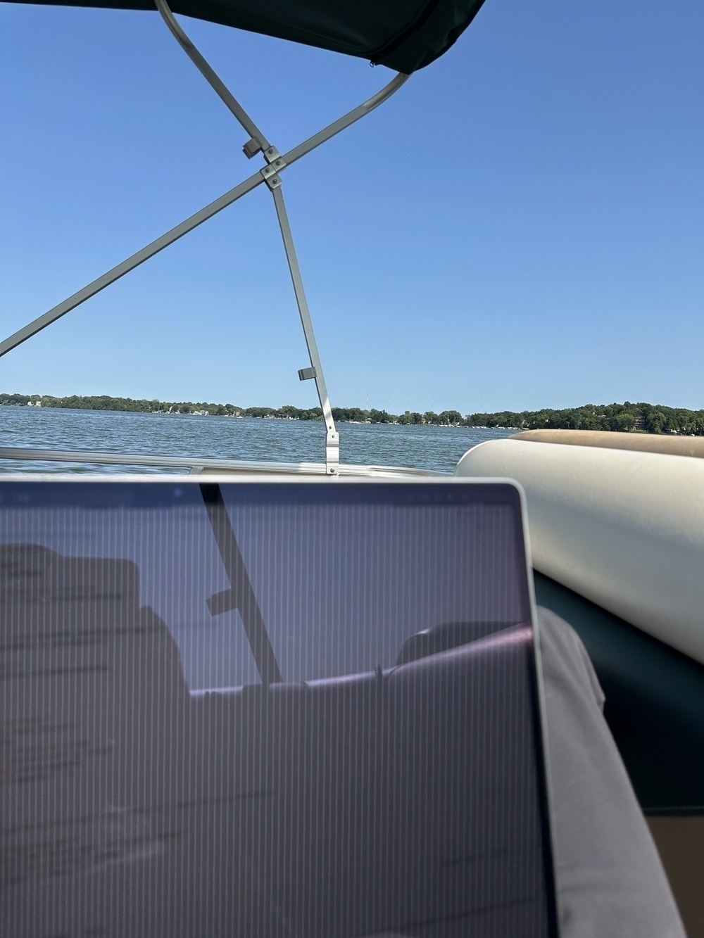 View of a lake from a boat, with a laptop screen reflecting the surroundings.