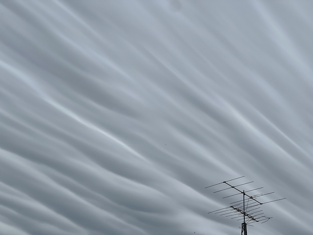streaks of grey clouds over an old school analog roof antenna. 
