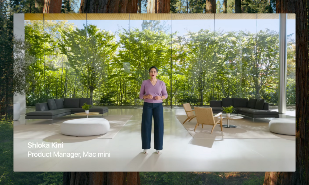 A woman stands and speaks in a modern, glass-walled room with outdoor greenery visible. Furnishings include sofas and round tables. Text reads: “Shloka Kini, Product Manager, Mac mini.”