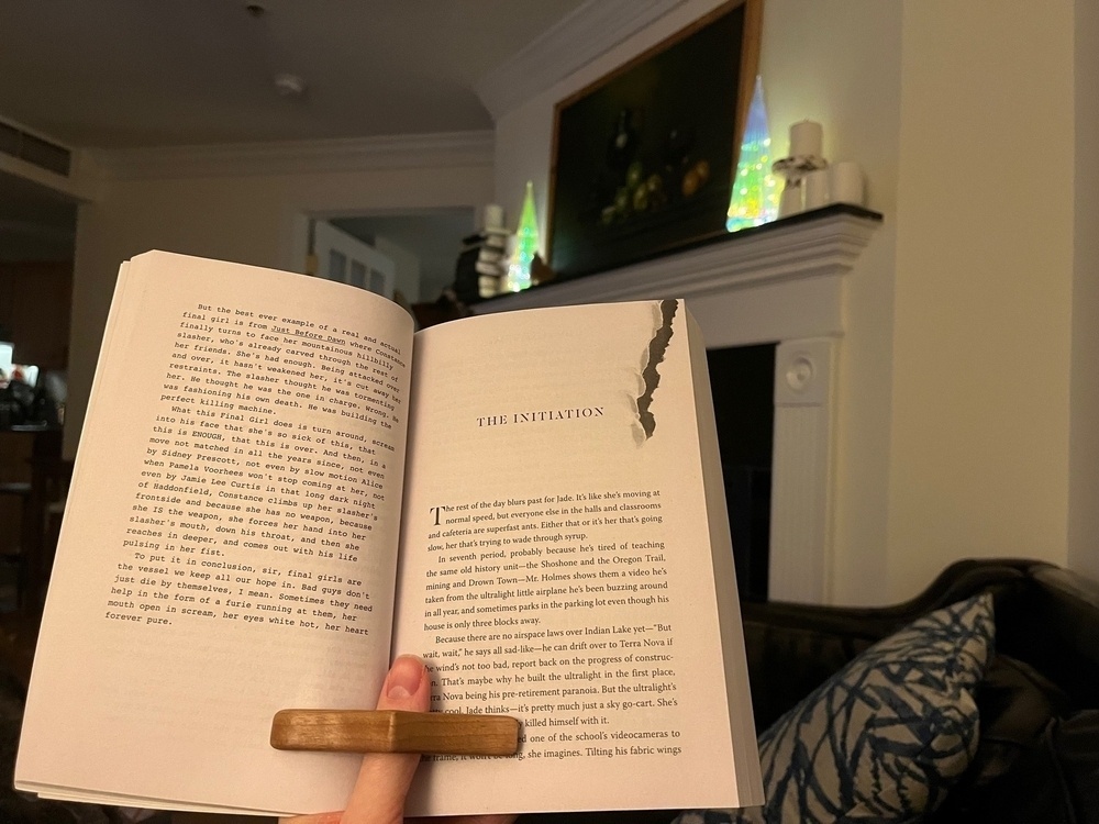 A book spread open in front of a hearth. Two long, conical, prismatic holiday decorations glow on the mantle.