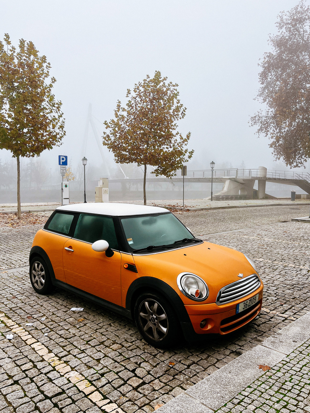 An orange Mini Cooper car parked, misty morning. 