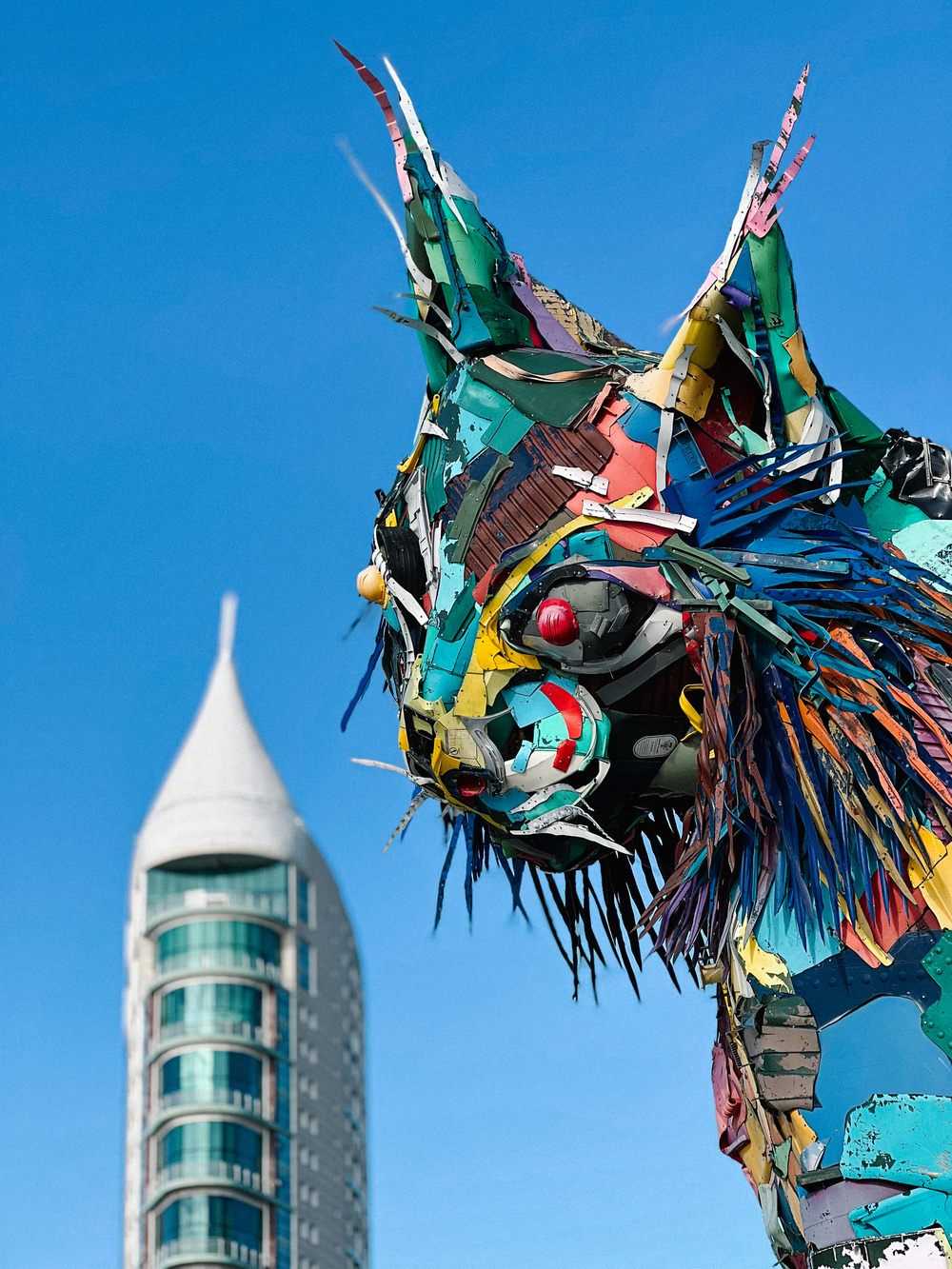 A giant sculpture of a cat, with a pointy building in the back.