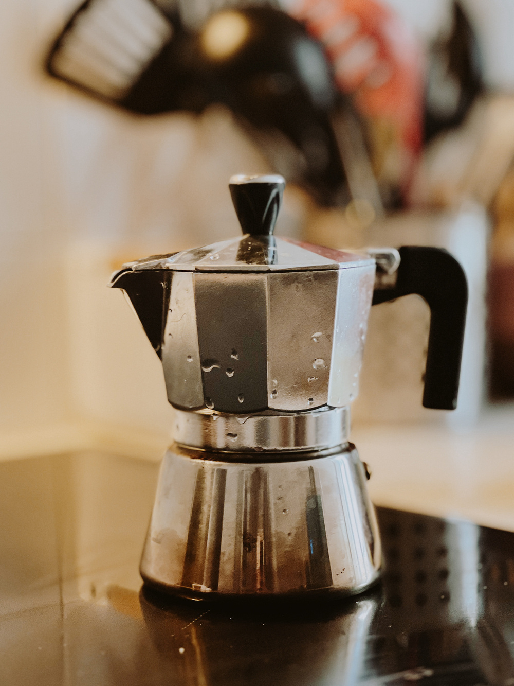 Moka pot on a stove with water droplets on the surface, suggesting recent use or boiling.