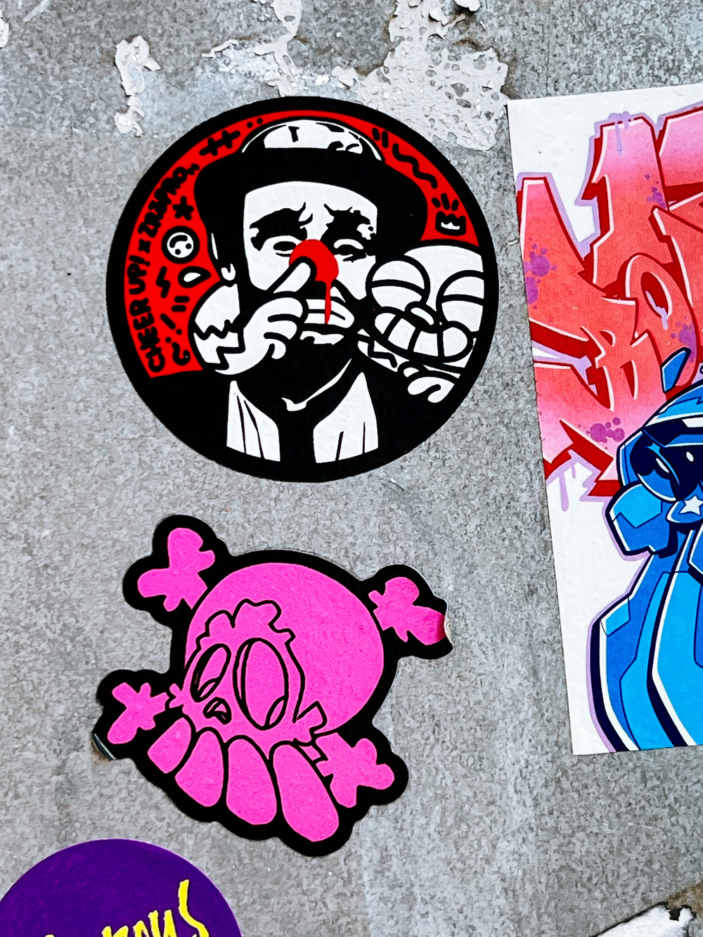 A two sticker combo. One has a robot like creature sticking a finger up a clown’s red nose (yup, true), and the other one is a pink skull & bones, with what looks like overdeveloped teeth (yup, true again).