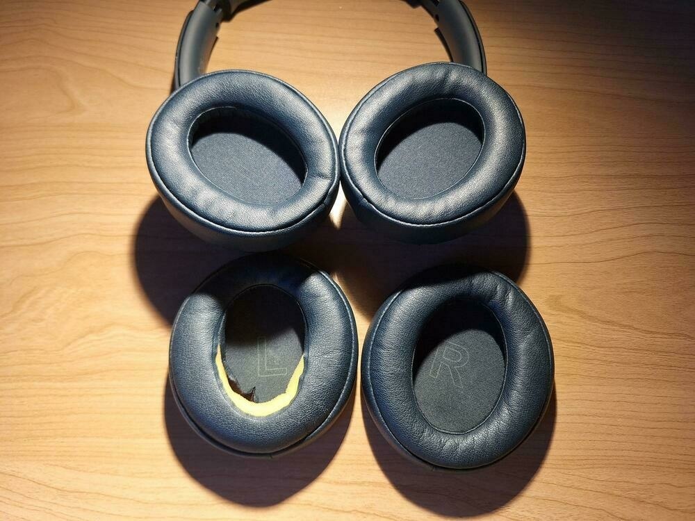 A picture of over-ear headphones with new replacement ear pads. In front are two original ear pads, one of it broken.