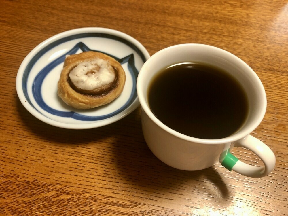 Cinnamon bun on a dish beside a cup of black coffee