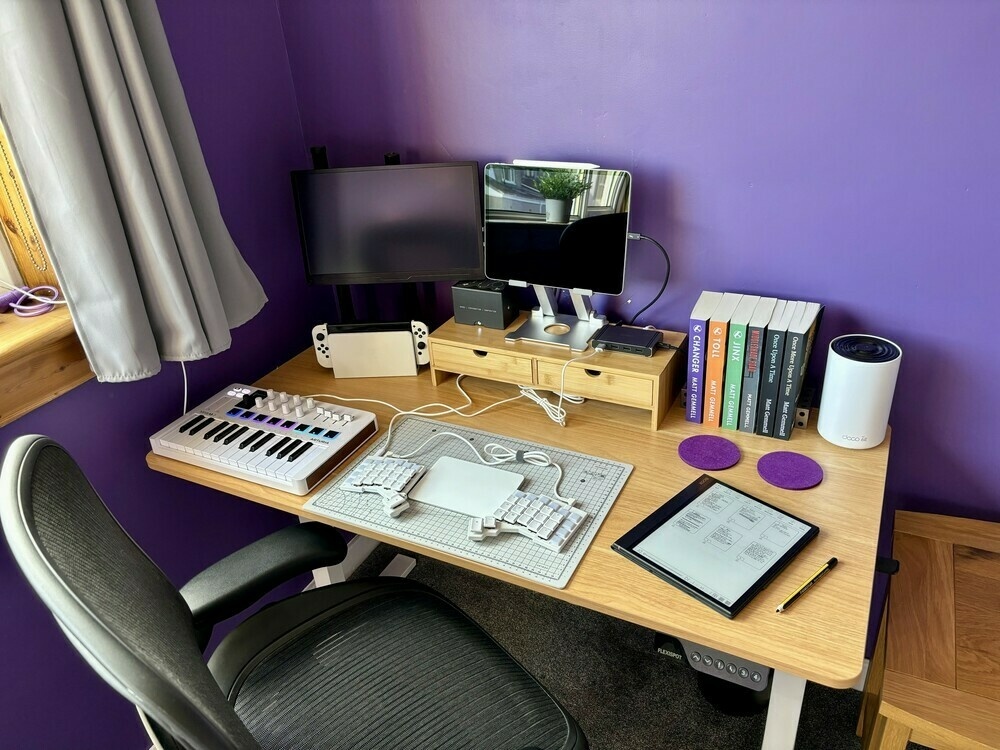 Desk with ipad pro, e-ink tablet, my books, nintendo switch and monitor, my voyager split keyboard and magic trackpad, and my new Arturia midi controller.